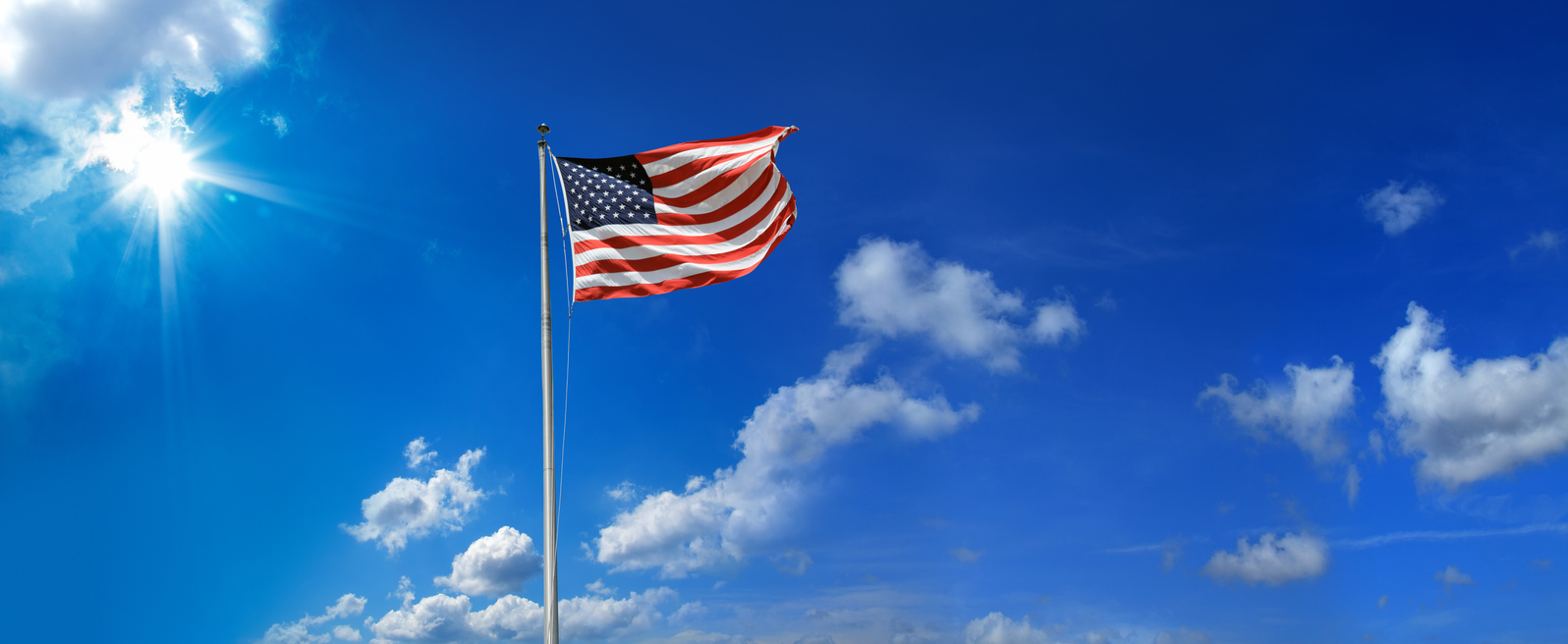 An American flag waving on a pole against a bright blue sky